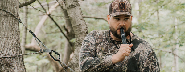 Man in camouflage clothing and a cap, holding the IronBuck, in a forest setting.