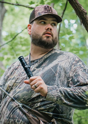 Man in camouflage clothing and cap holding the IronBuck in a forest setting